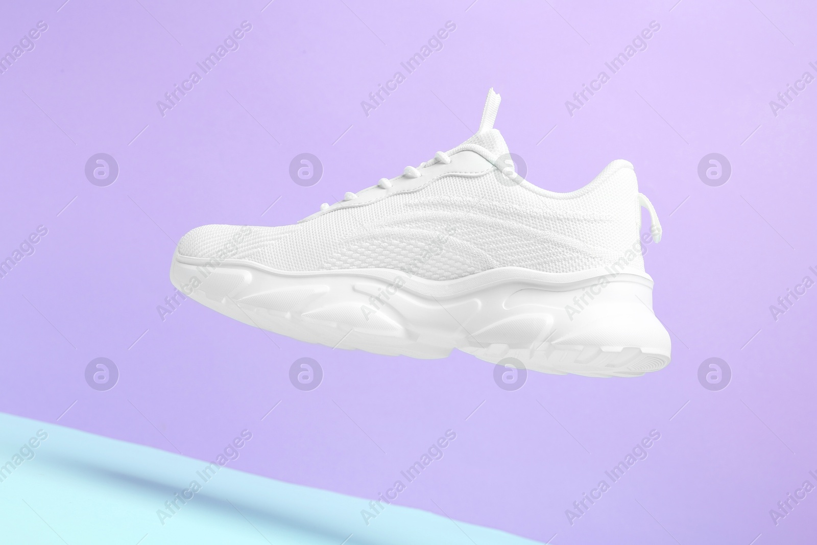 Photo of Stylish white sneaker in air against color background