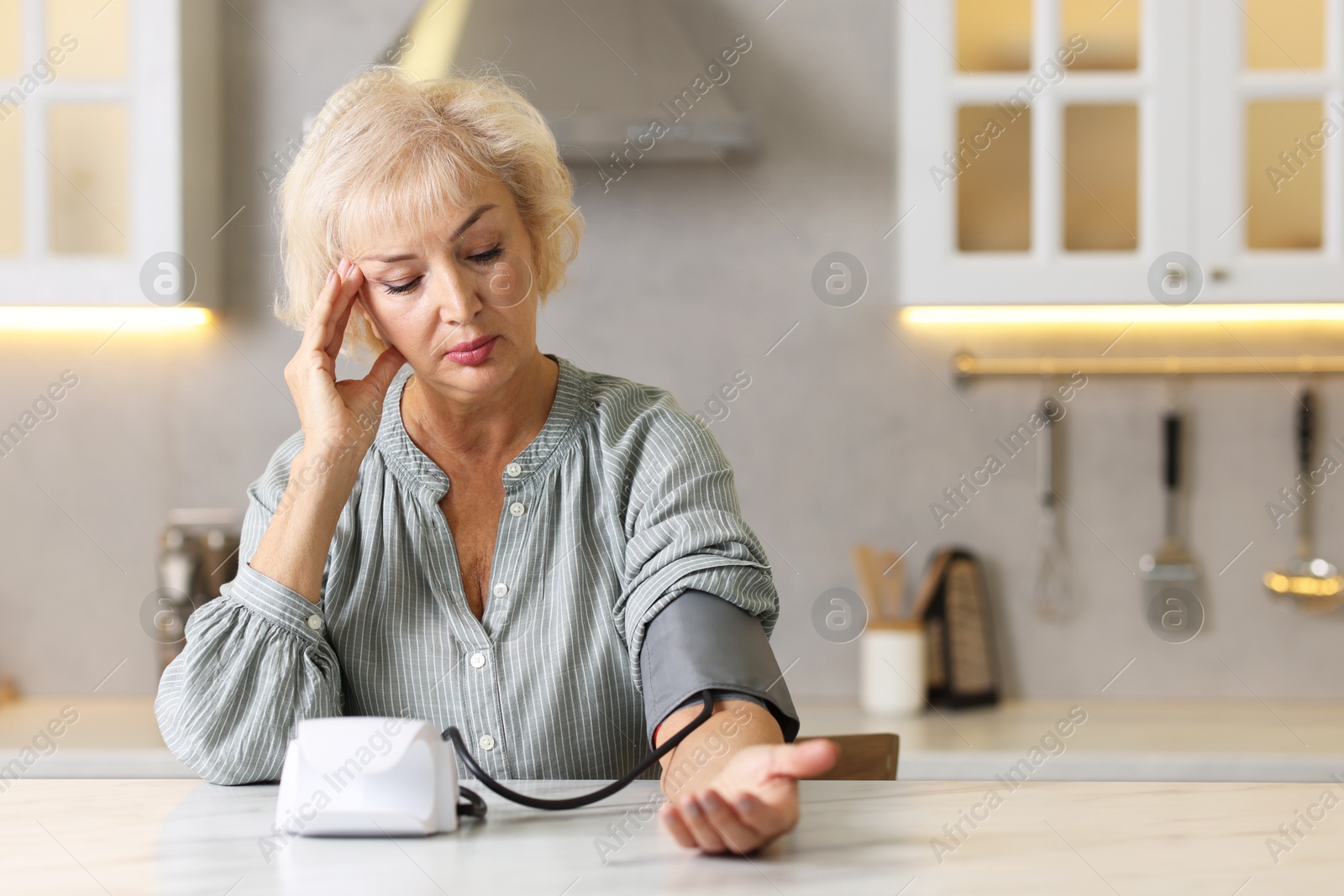 Photo of Senior woman measuring blood pressure at table in kitchen. Space for text