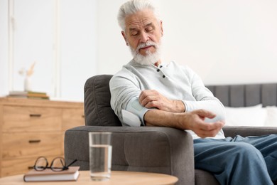 Photo of Senior man measuring blood pressure in armchair at home