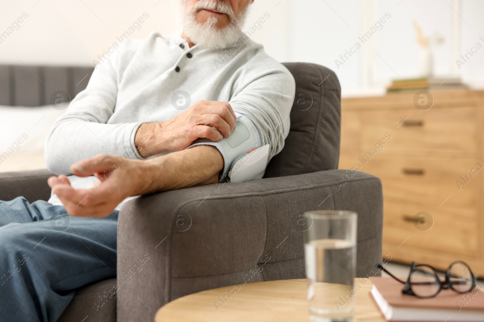 Photo of Senior man measuring blood pressure in armchair at home, closeup