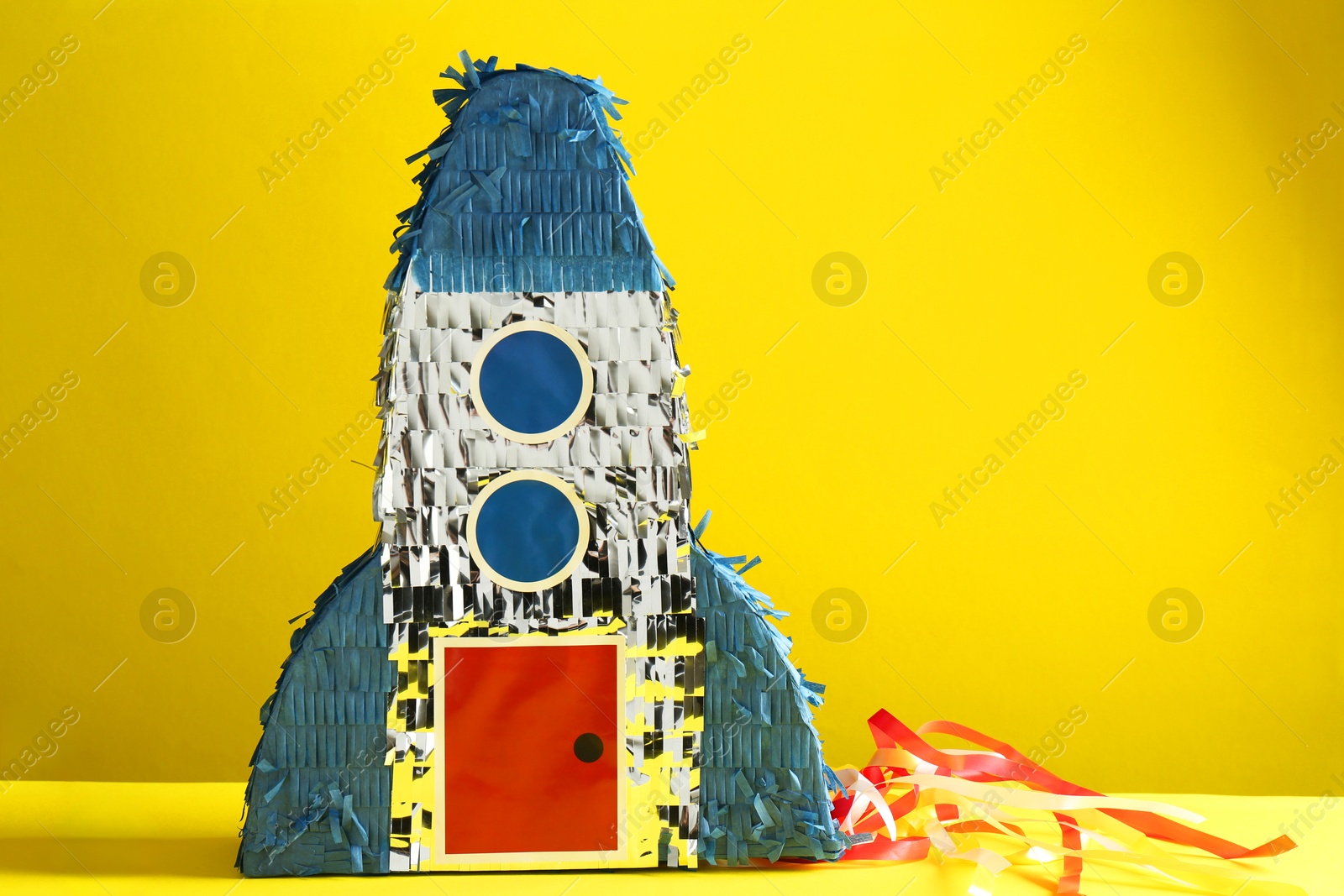 Photo of Bright pinata in shape of spaceship on yellow background. Space for text