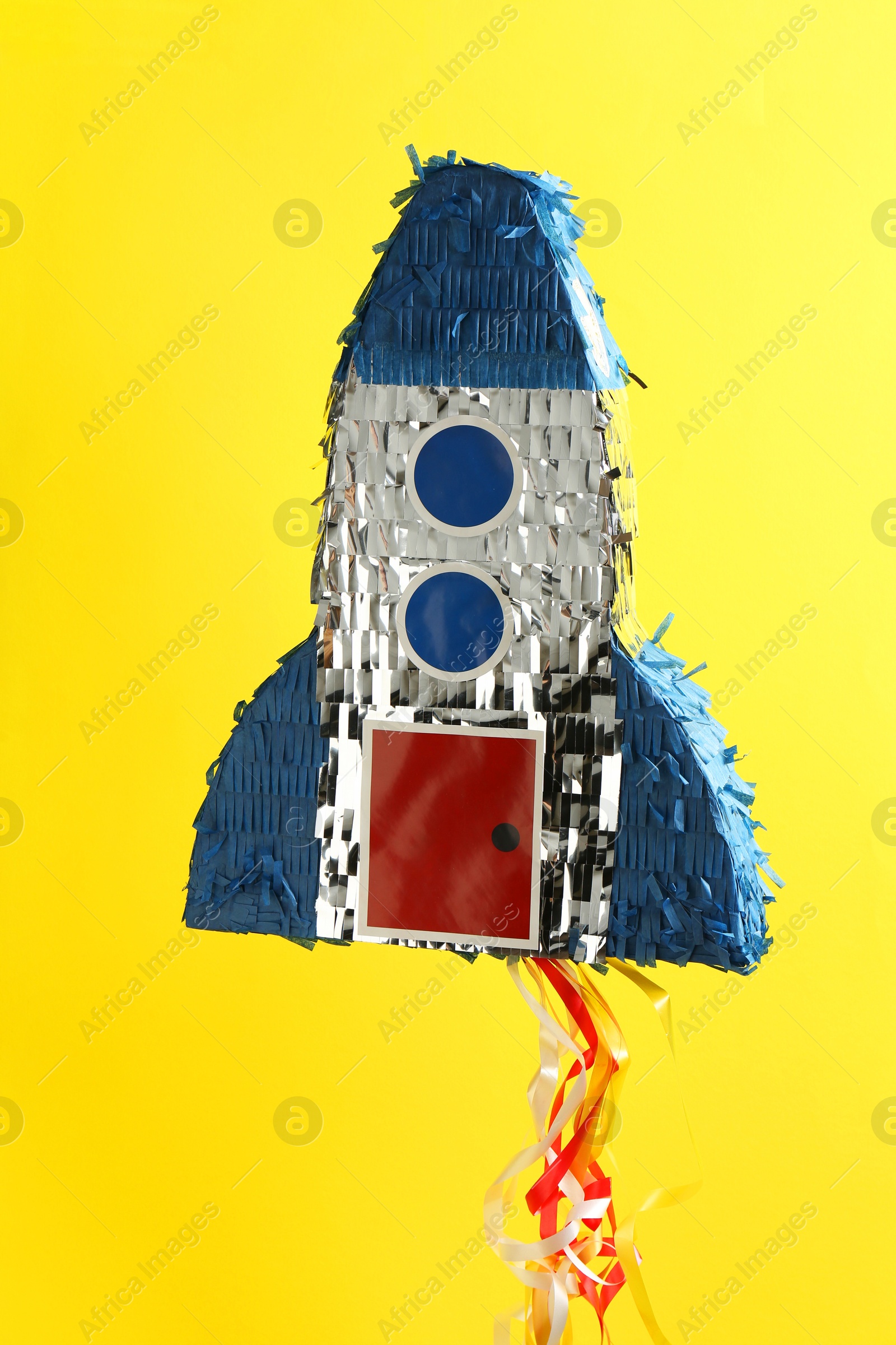 Photo of Bright pinata in shape of spaceship hanging on yellow background