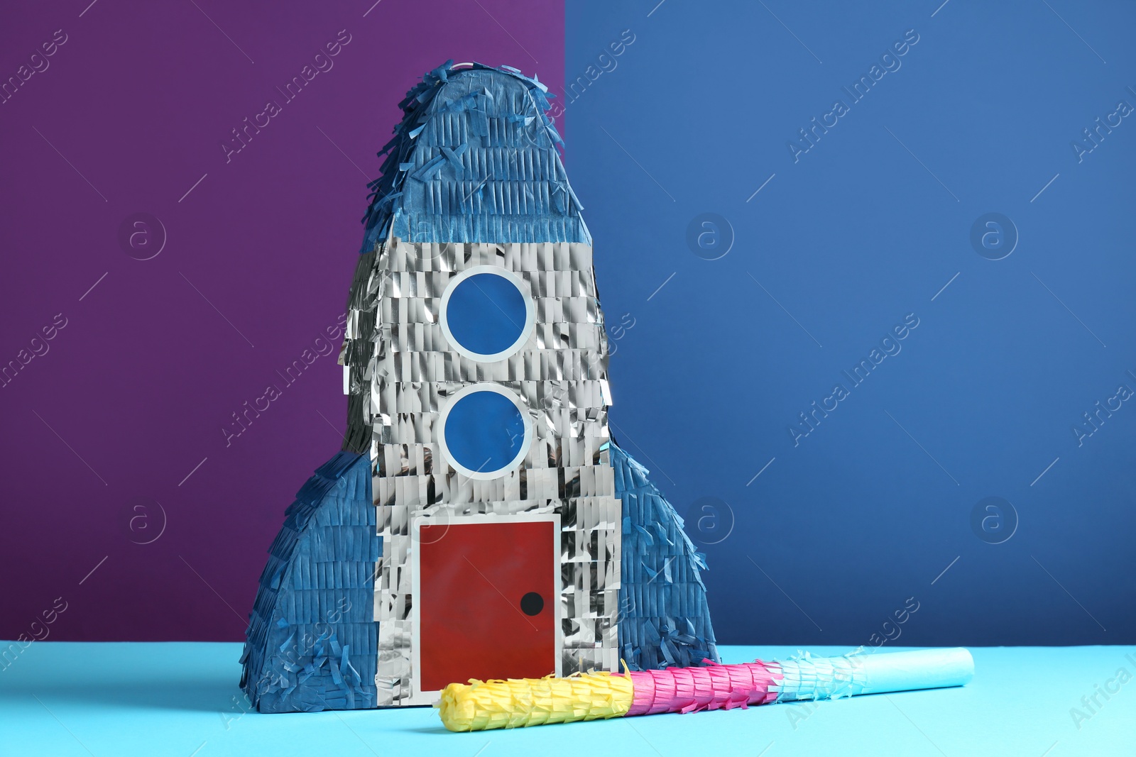 Photo of Bright pinata in shape of spaceship and stick on color background. Space for text