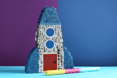 Photo of Bright pinata in shape of spaceship and stick on color background. Space for text