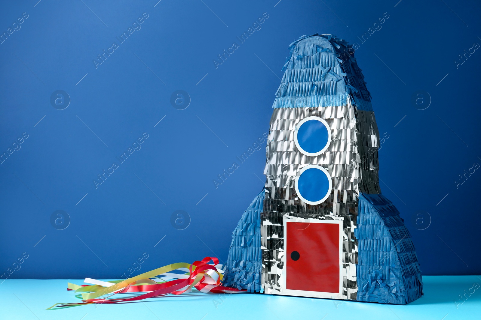 Photo of Bright pinata in shape of spaceship on blue background. Space for text