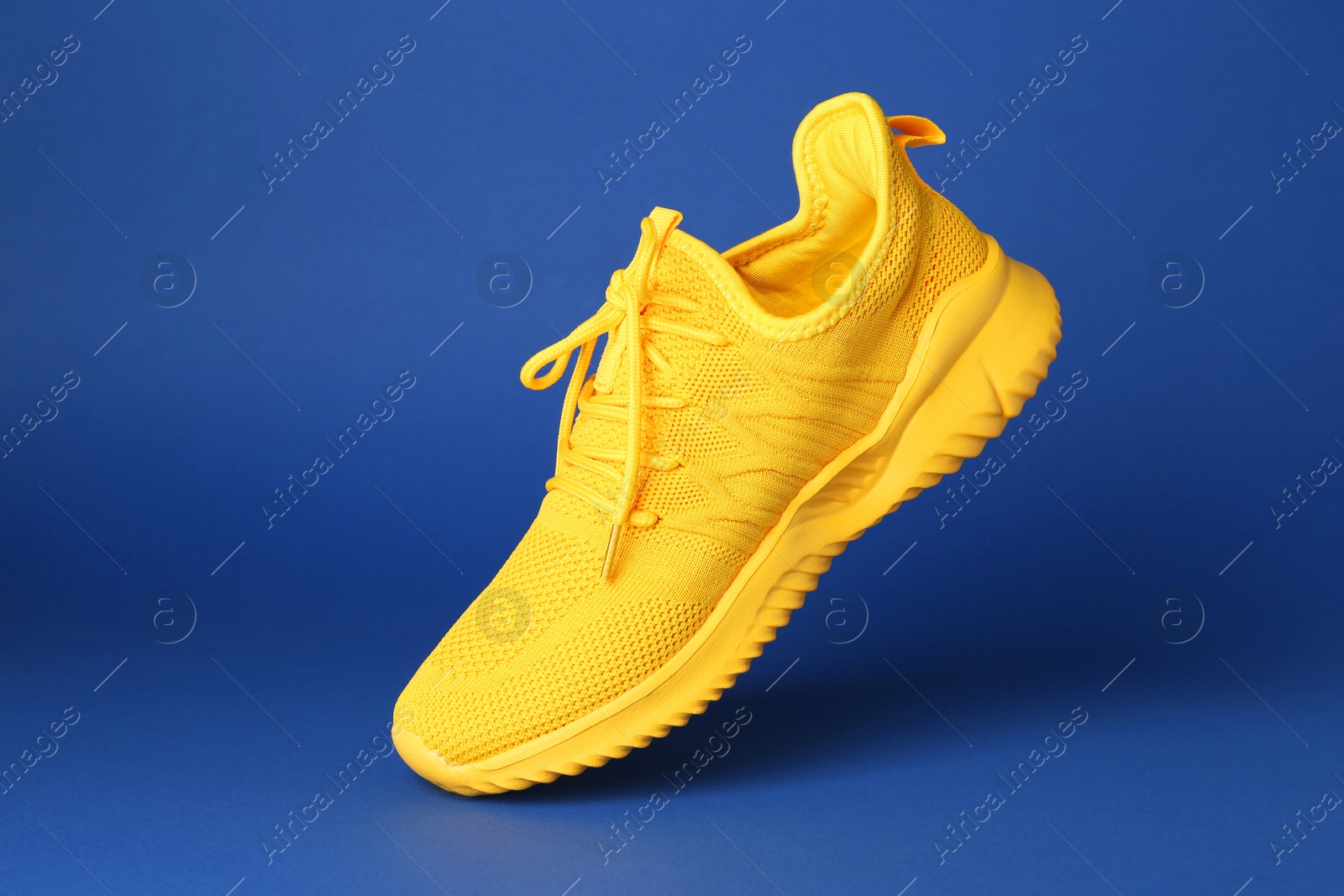 Photo of Stylish yellow sneaker in air against blue background