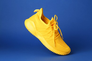 Photo of Stylish yellow sneaker in air against blue background