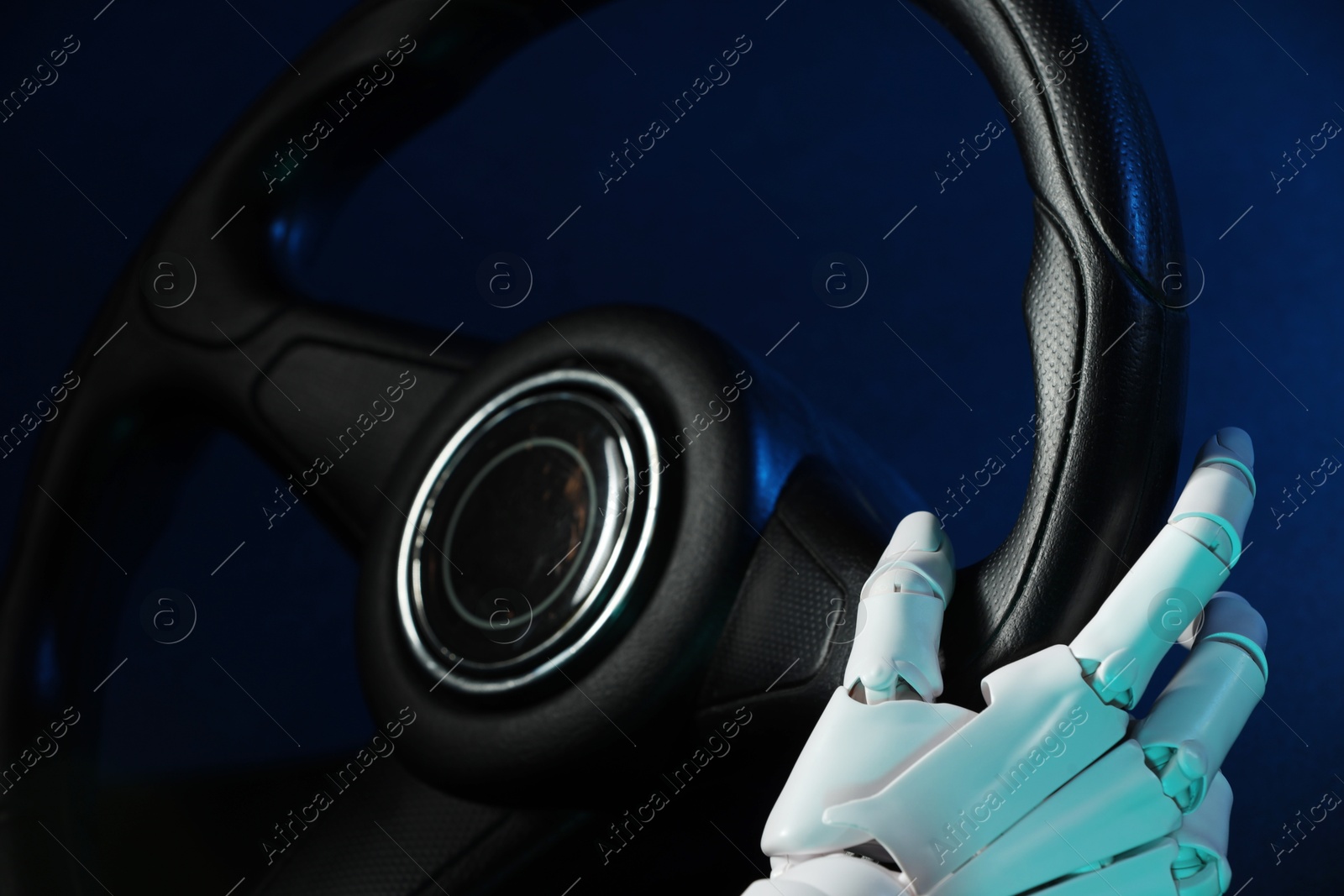 Photo of Artificial intelligence. Robot hand with steering wheel on dark blue background, closeup