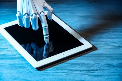 Photo of Artificial intelligence. Robot hand using tablet at wooden table, closeup