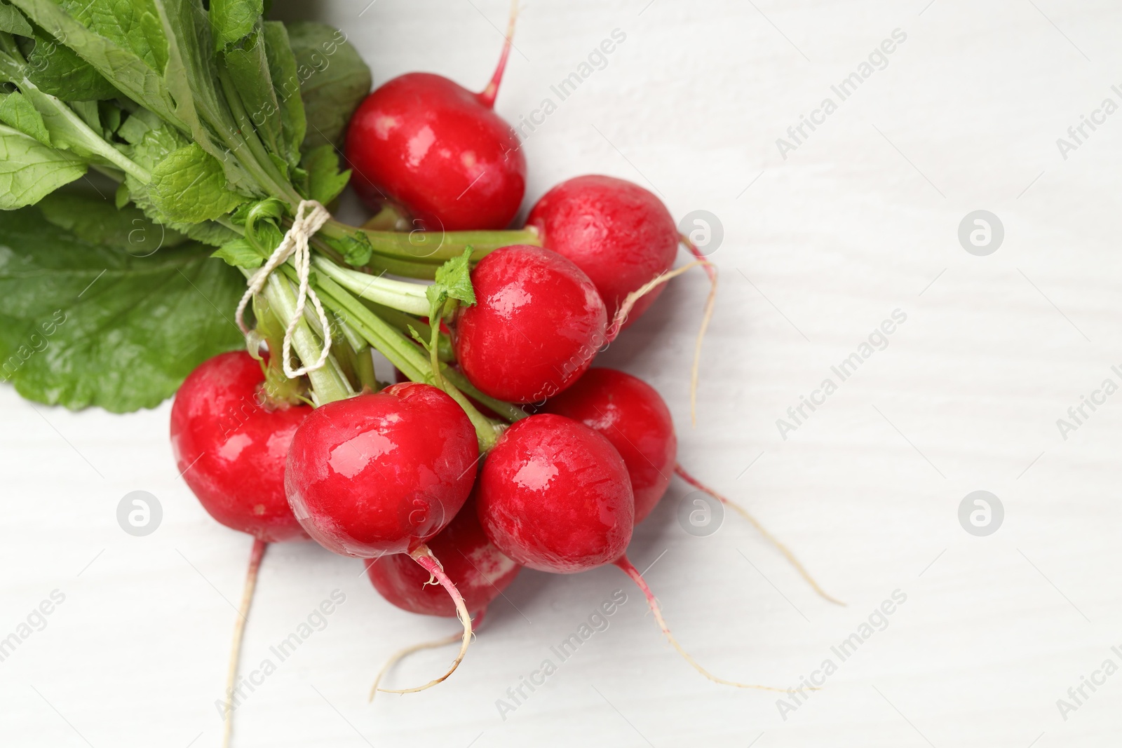 Photo of Bunch of fresh radishes on white wooden table, top view. Space for text