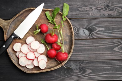 Photo of Many fresh radishes and knife on black wooden table, top view. Space for text