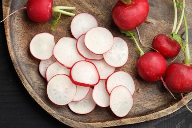 Photo of Fresh whole and cut radishes on black wooden table, top view