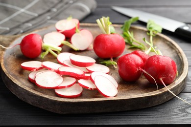 Photo of Fresh whole and cut radishes on black wooden table, closeup