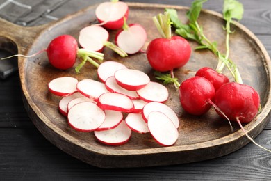 Photo of Fresh whole and cut radishes on black wooden table, closeup
