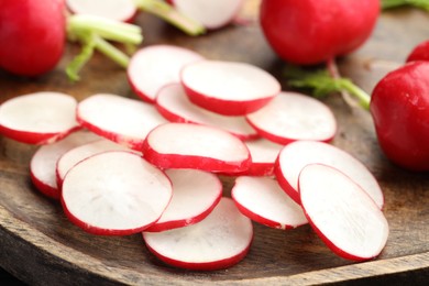 Photo of Fresh whole and cut radishes on wooden board, closeup