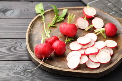 Photo of Fresh whole and cut radishes on black wooden table, closeup