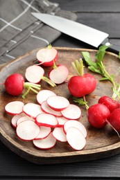 Photo of Fresh whole and cut radishes on black wooden table, closeup