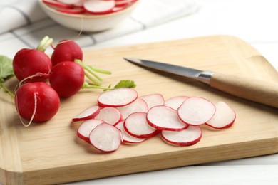 Photo of Many fresh radishes and knife on white wooden table, closeup