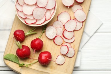 Photo of Fresh whole and cut radishes on white wooden table, top view