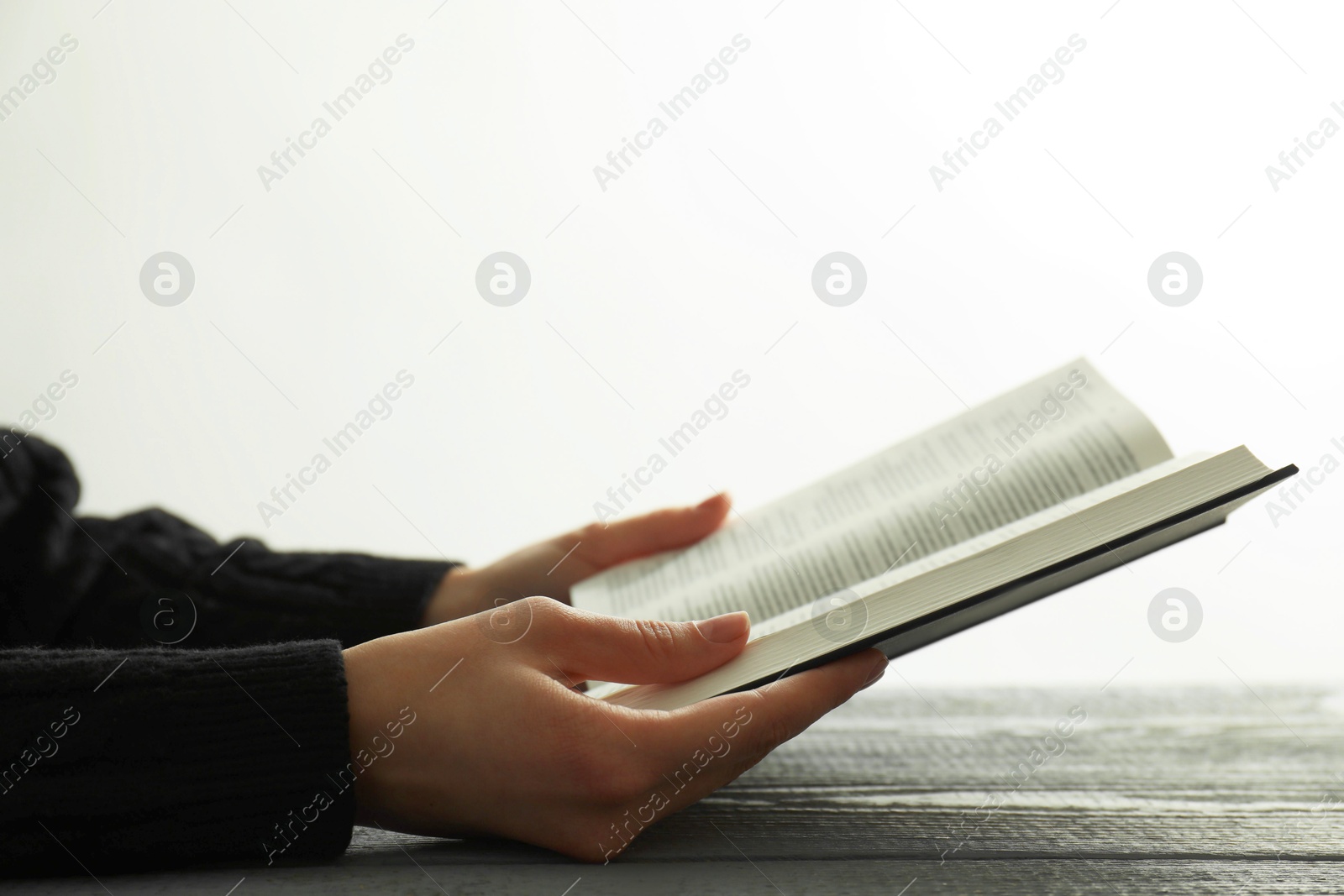 Photo of Woman with open Holy Bible at wooden table, closeup