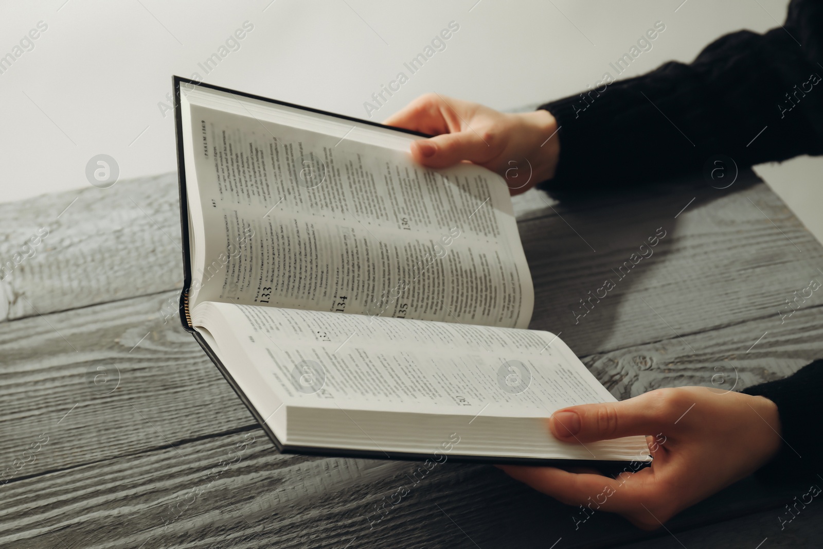 Photo of Woman with open Holy Bible in English language at wooden table, closeup