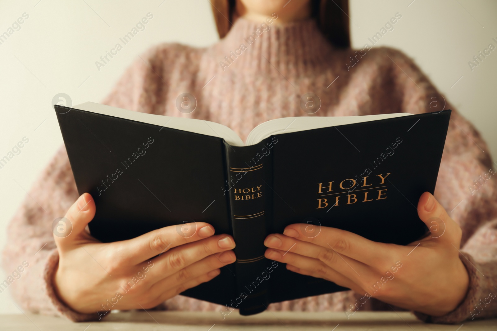 Photo of Woman reading Holy Bible at table, closeup