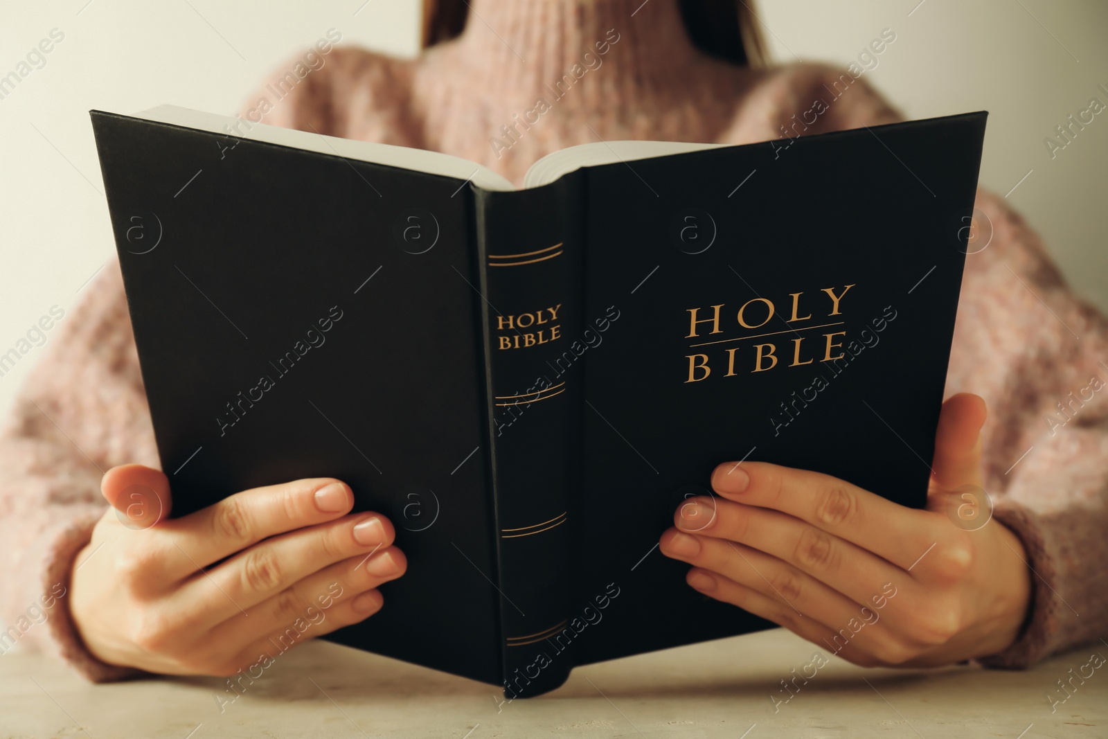 Photo of Woman reading Holy Bible at beige table, closeup