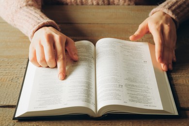 Photo of Woman reading Holy Bible in English language at wooden table, closeup