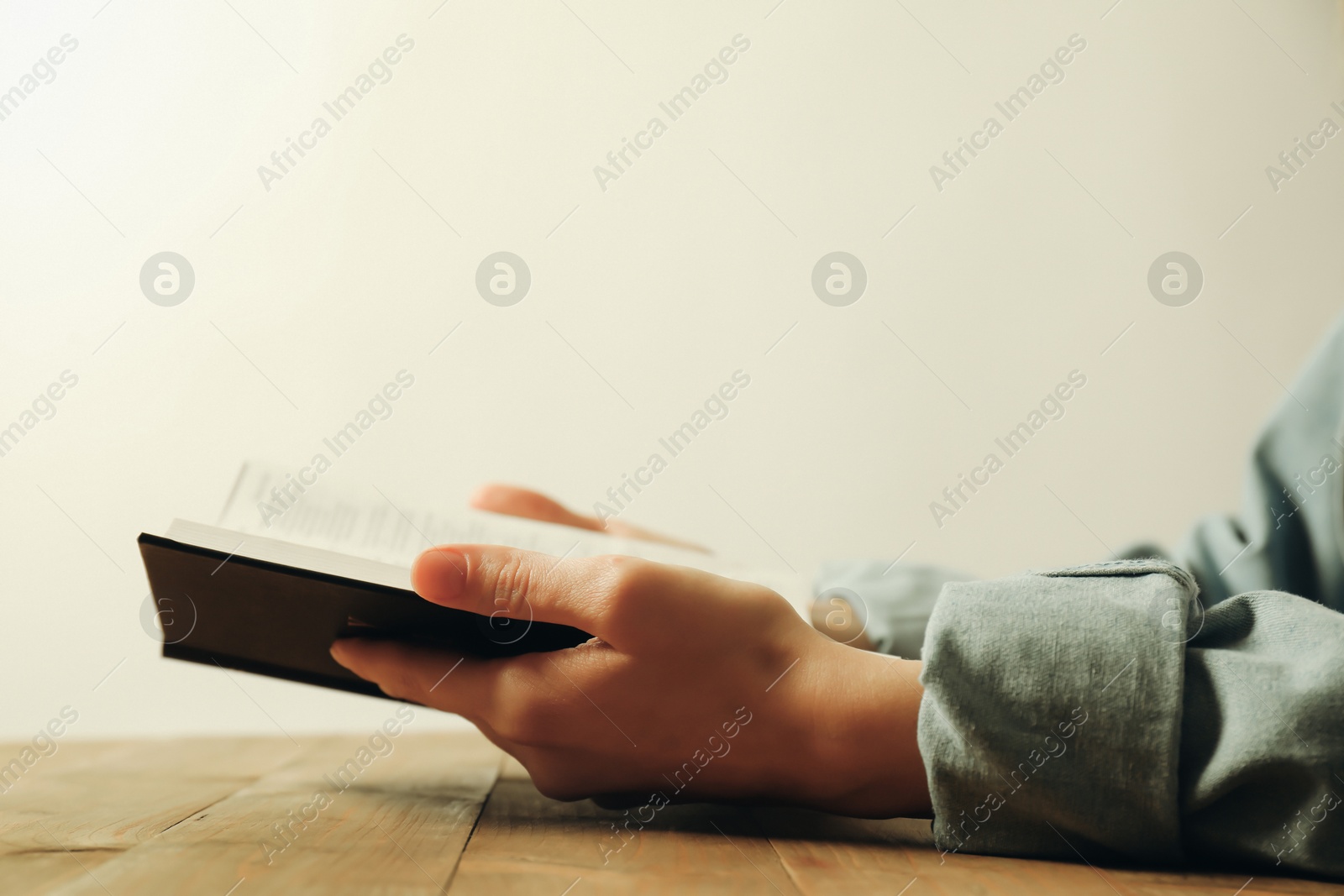 Photo of Woman reading Holy Bible at wooden table, closeup