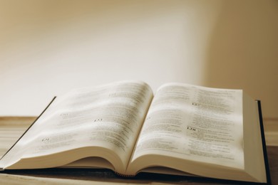 Photo of Open Holy Bible in English language on beige table, closeup