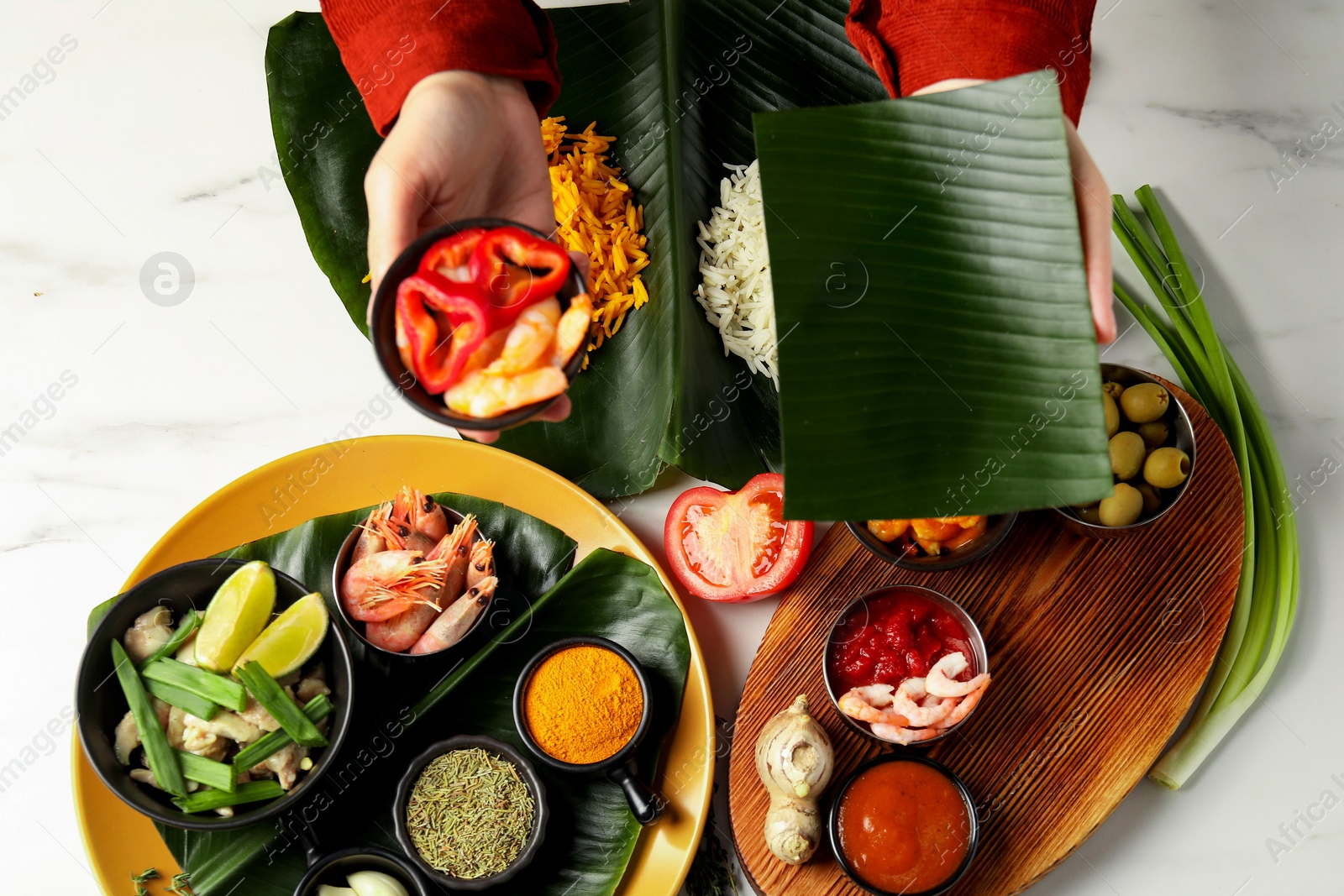 Photo of Woman holding piece of banana leaf and bowl with shrimps at white marble table, top view