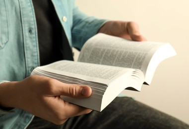 Man reading Holy Bible in English language on light background, closeup