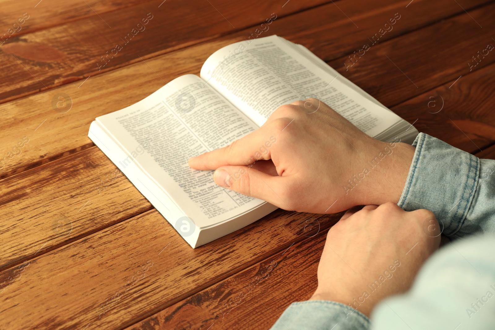 Photo of Man reading Holy Bible in English language at wooden table, closeup