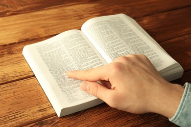 Photo of Man reading Holy Bible in English language at wooden table, closeup