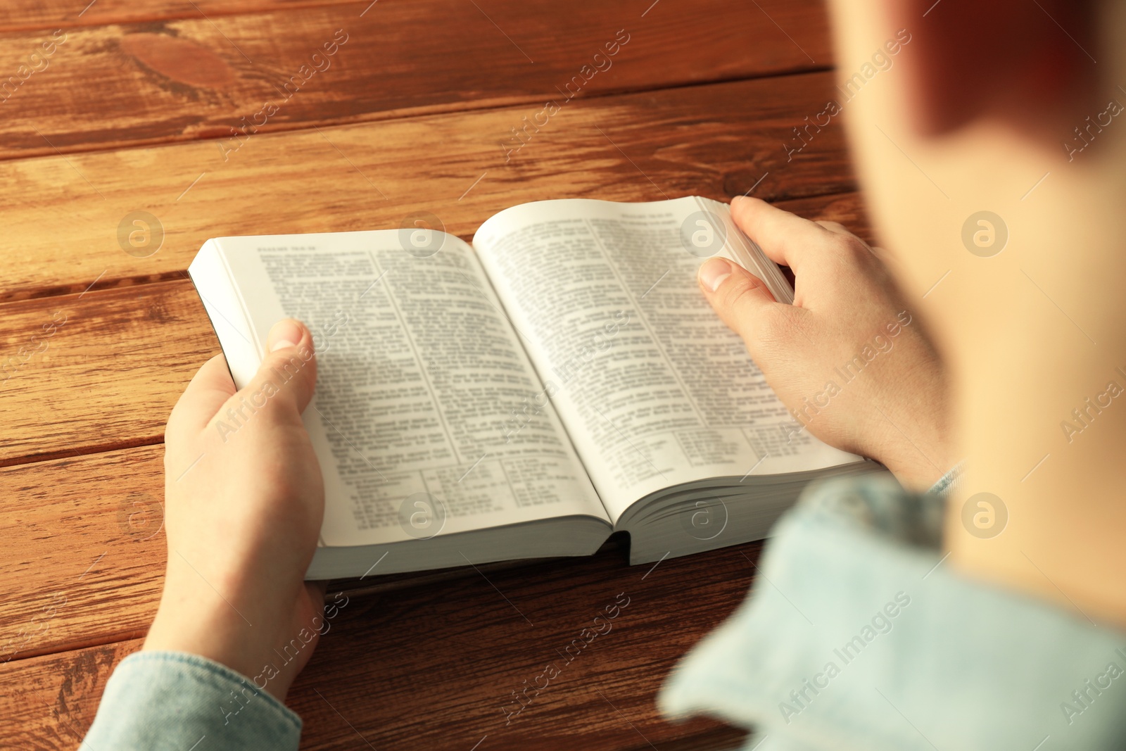 Photo of Man reading Holy Bible in English language at wooden table, closeup