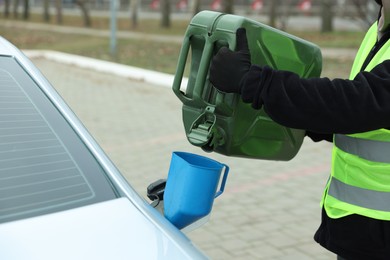 Photo of Man pouring fuel from canister into funnel outdoors, closeup