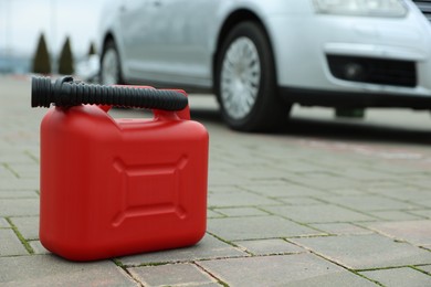 Photo of Red plastic canister with spout on pavement outdoors