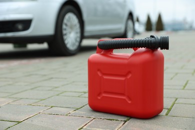 Photo of Red plastic canister with spout on pavement outdoors