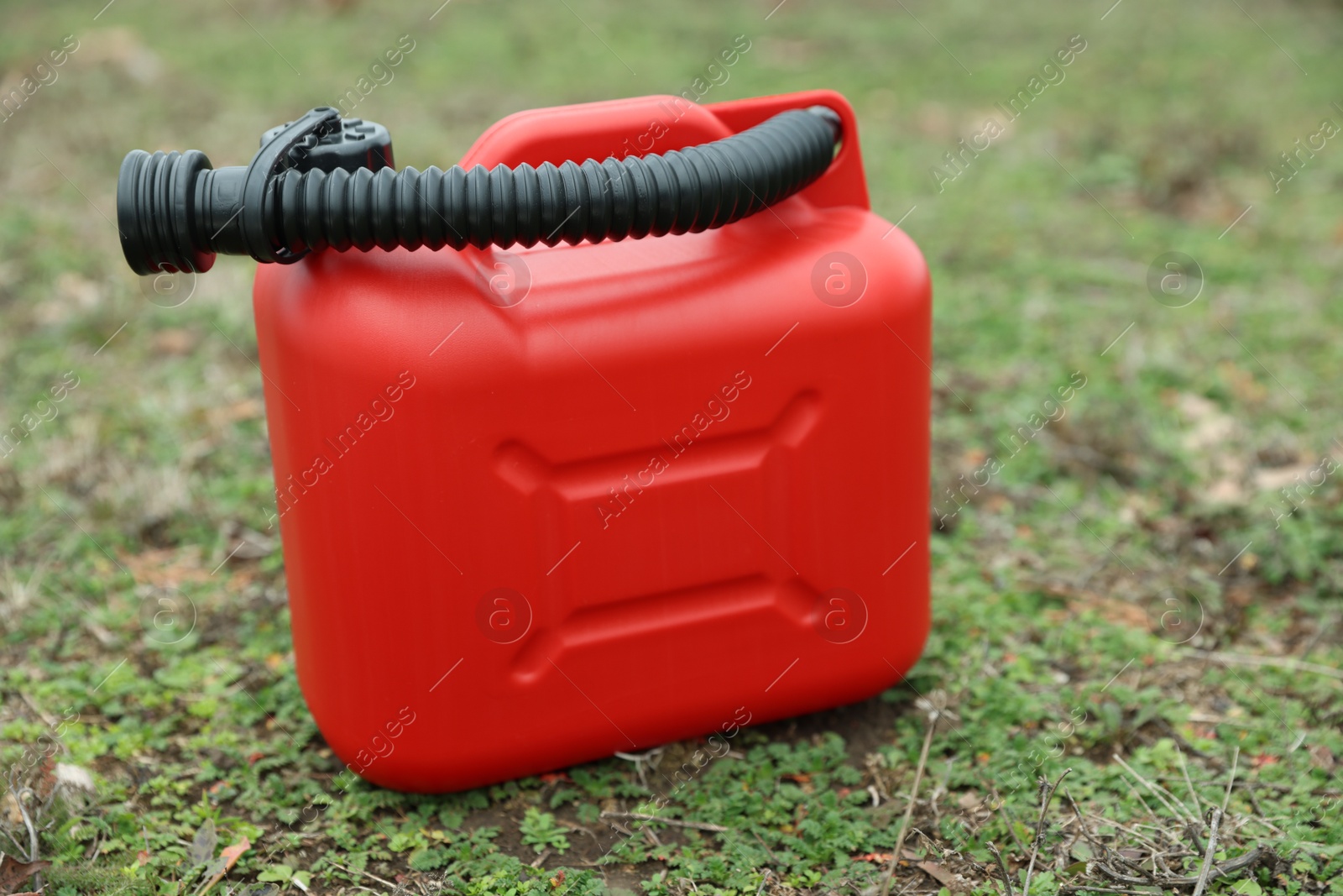 Photo of Red plastic canister with spout on green grass outdoors