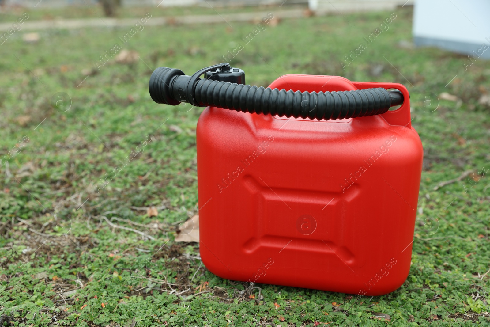 Photo of Red plastic canister with spout on green grass outdoors