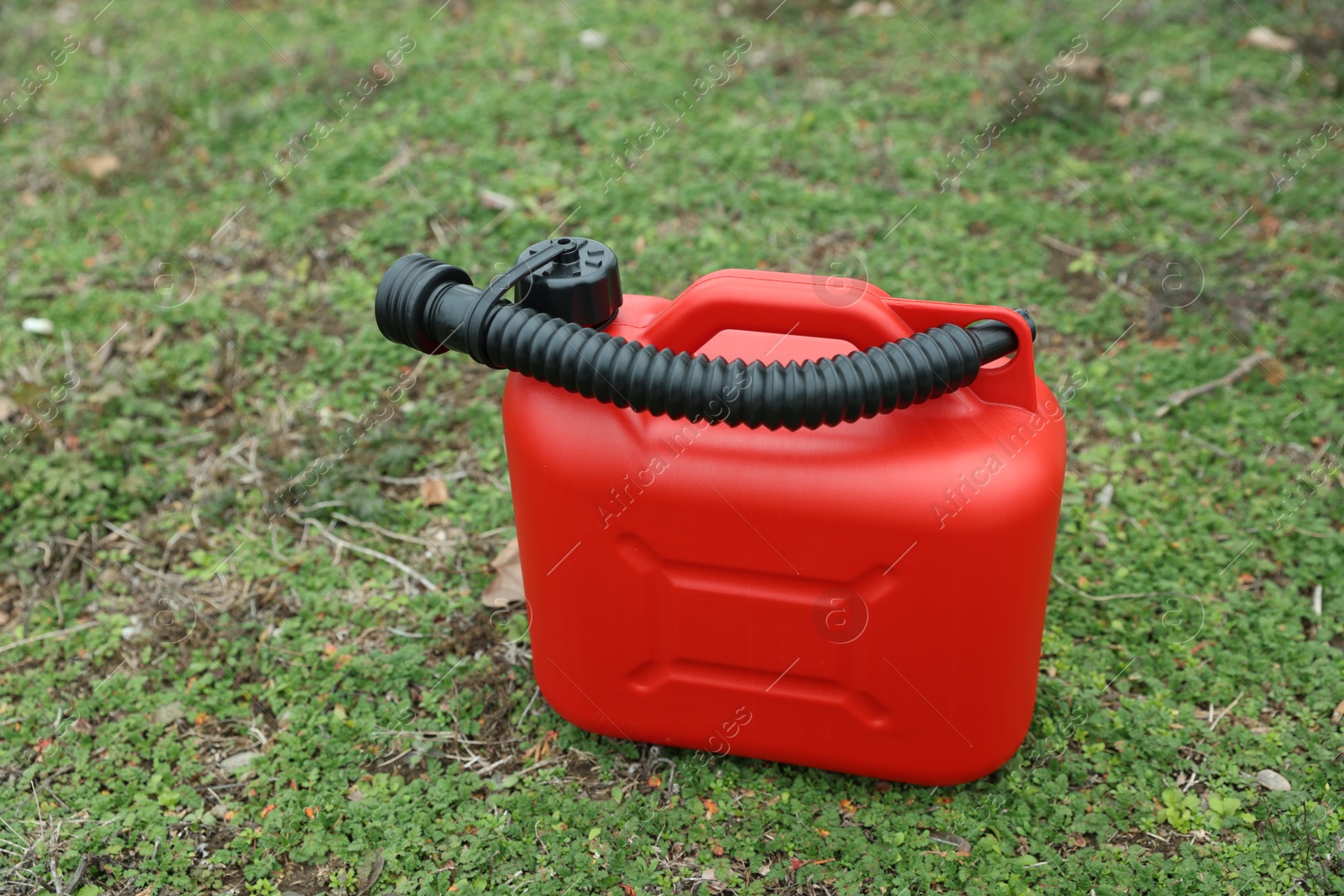 Photo of Red plastic canister with spout on green grass outdoors