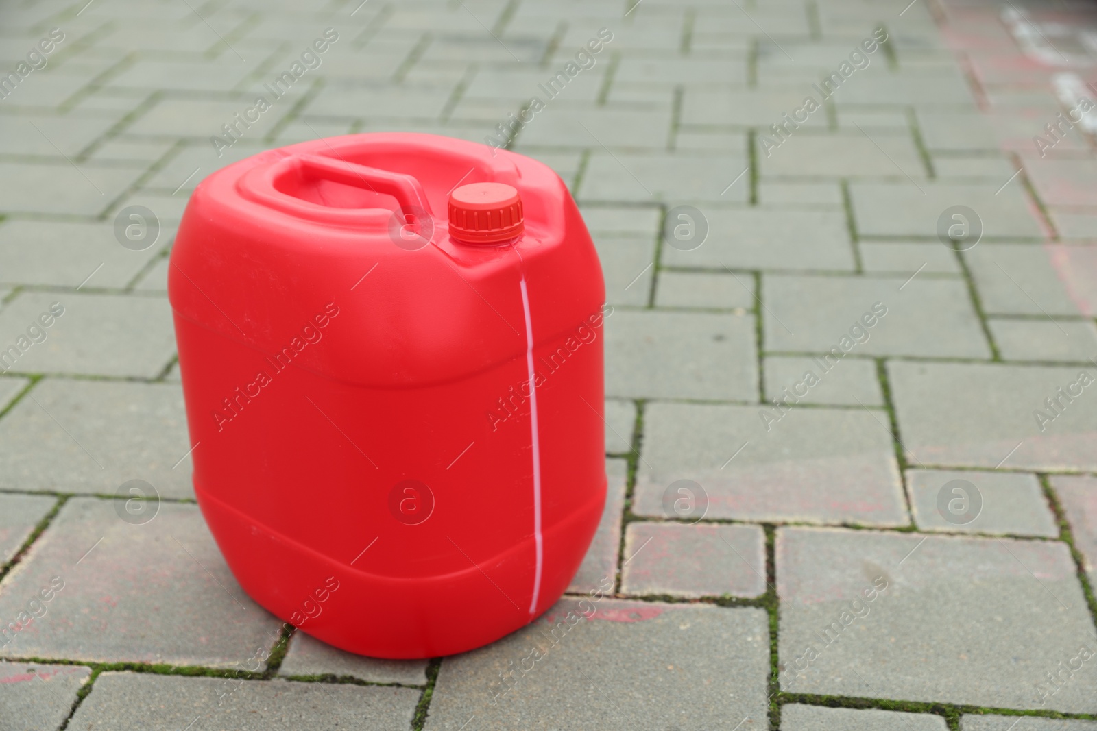 Photo of One red plastic canister on pavement outdoors, space for text