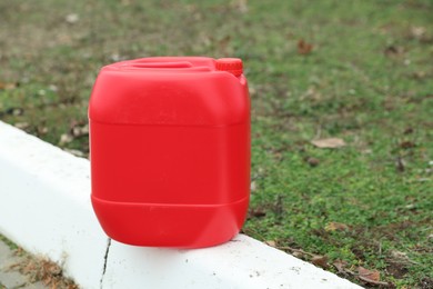 One red plastic canister on curb outdoors, space for text