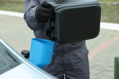 Photo of Man pouring fuel from canister into funnel outdoors, closeup