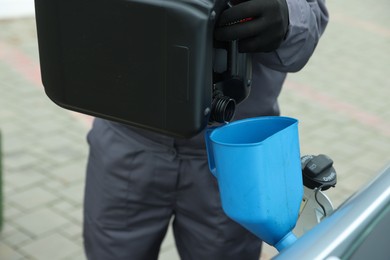 Photo of Man pouring fuel from canister into funnel outdoors, closeup