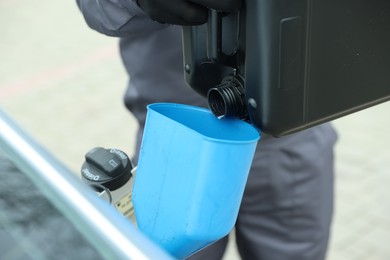 Photo of Man pouring fuel from canister into funnel outdoors, closeup