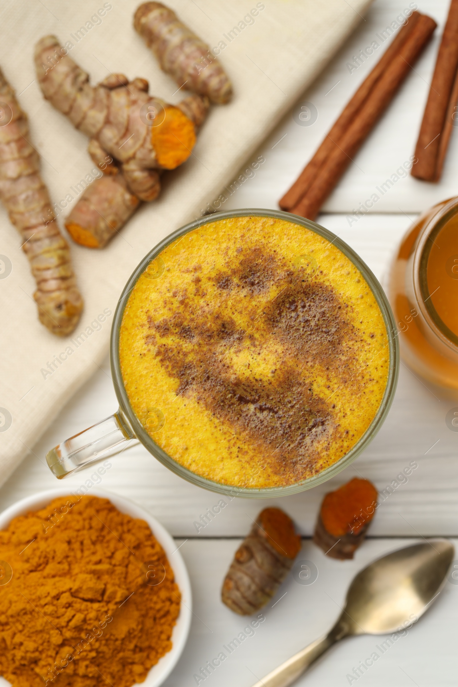 Photo of Tasty turmeric latte in cup and ingredients on white wooden table, flat lay