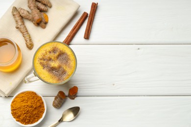 Photo of Tasty turmeric latte in cup and ingredients on white wooden table, flat lay. Space for text