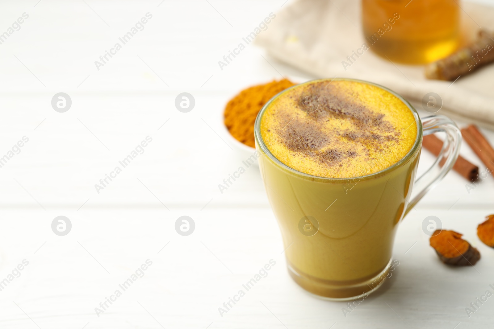 Photo of Tasty turmeric latte in cup and ingredients on white wooden table, closeup. Space for text