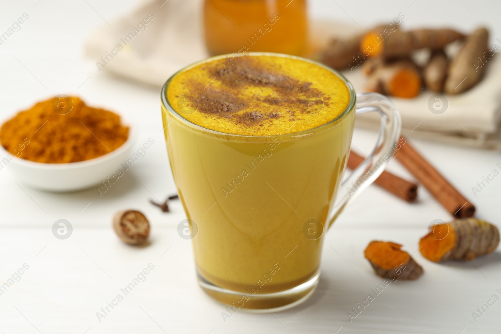 Photo of Tasty turmeric latte in cup and ingredients on white wooden table, closeup